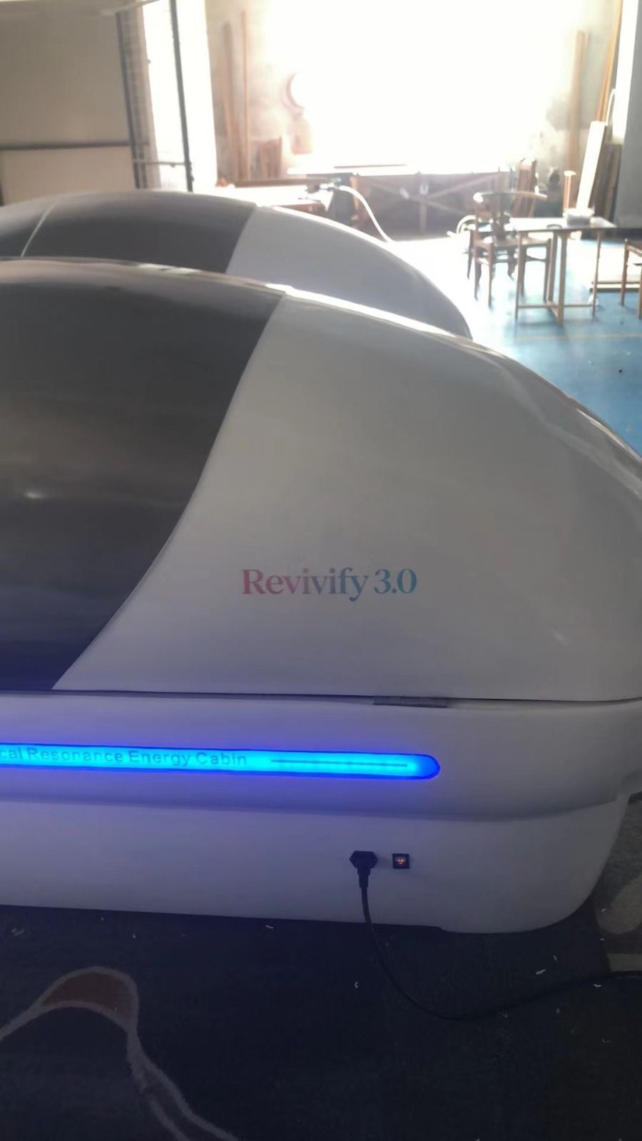 White and gray reclining therapy pod with blue light in a bright room