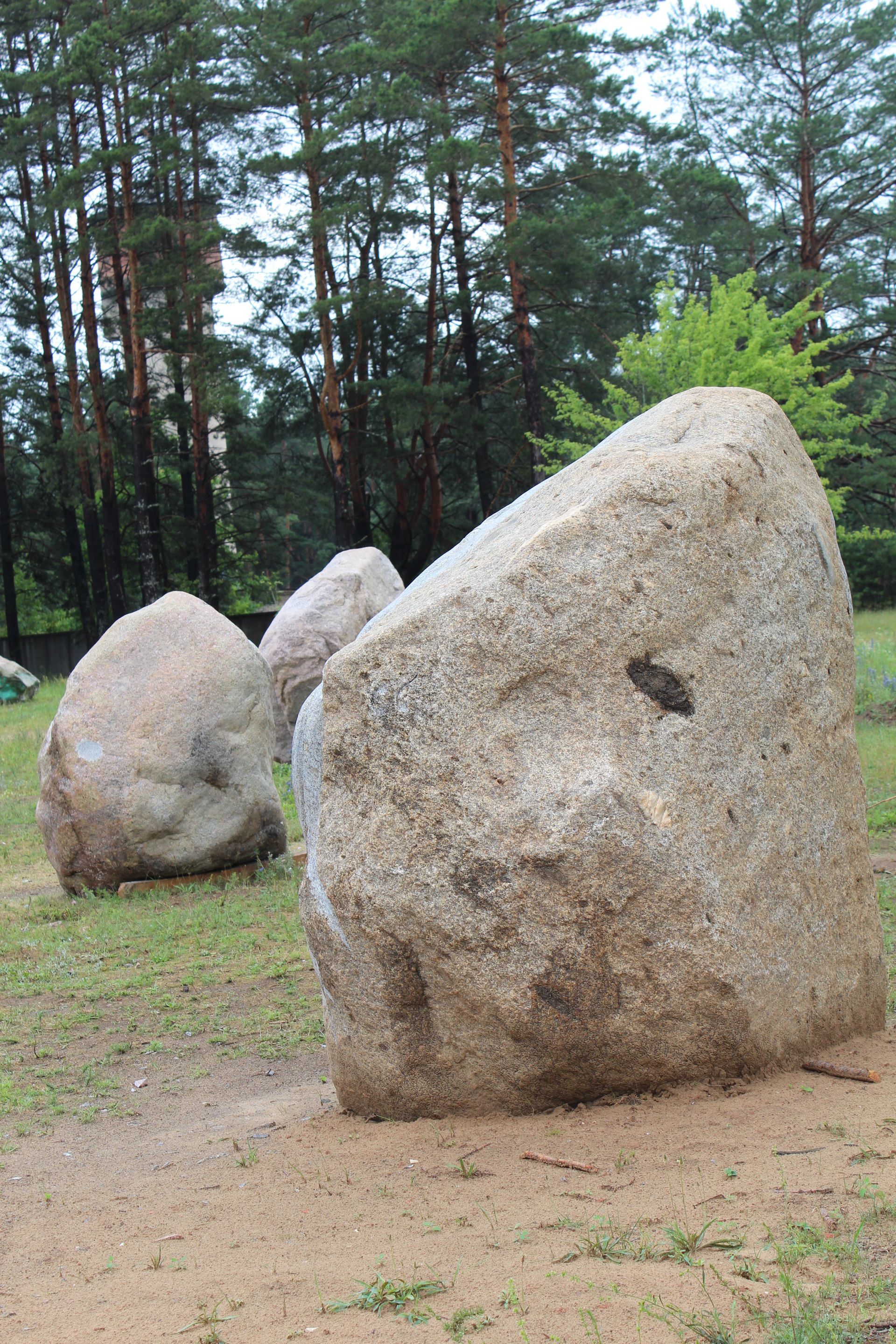 Three large, light-colored granite boulders on a grassy area, trees in the background.