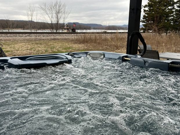 Bubbling hot tub outdoors with a train passing in the background on a cloudy day.