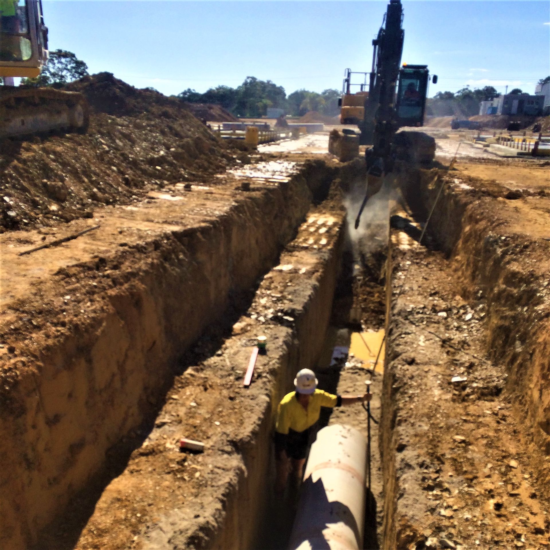 A man is standing in a trench next to a pipe
