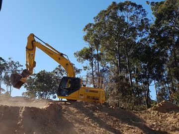 A large yellow excavator is digging a hole in the dirt.