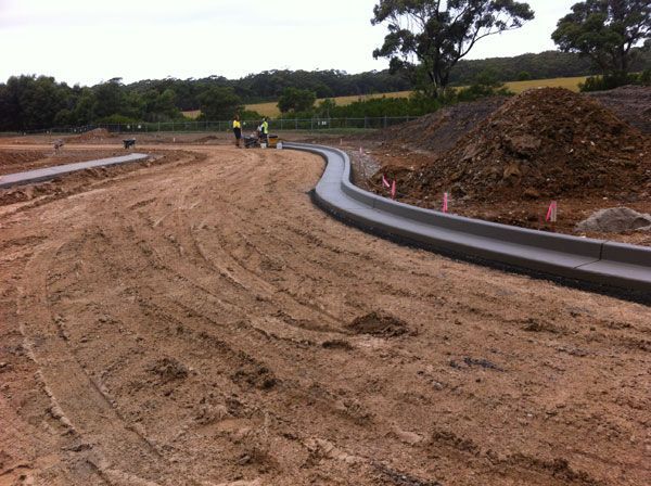 A concrete curb is being installed on a dirt road.