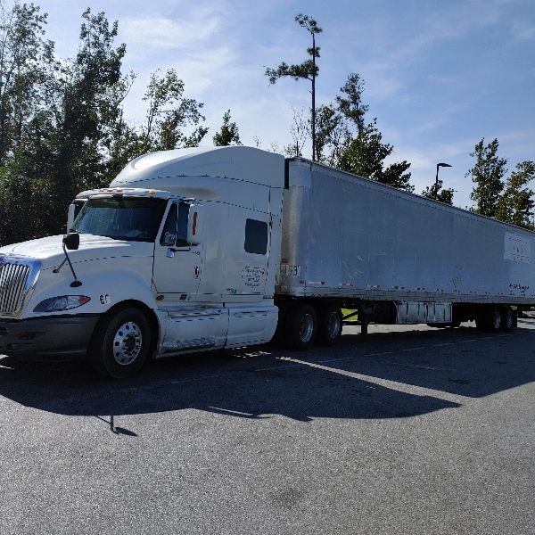 White semi-truck parked in a lot; trailer, cab and trees visible under a blue sky.