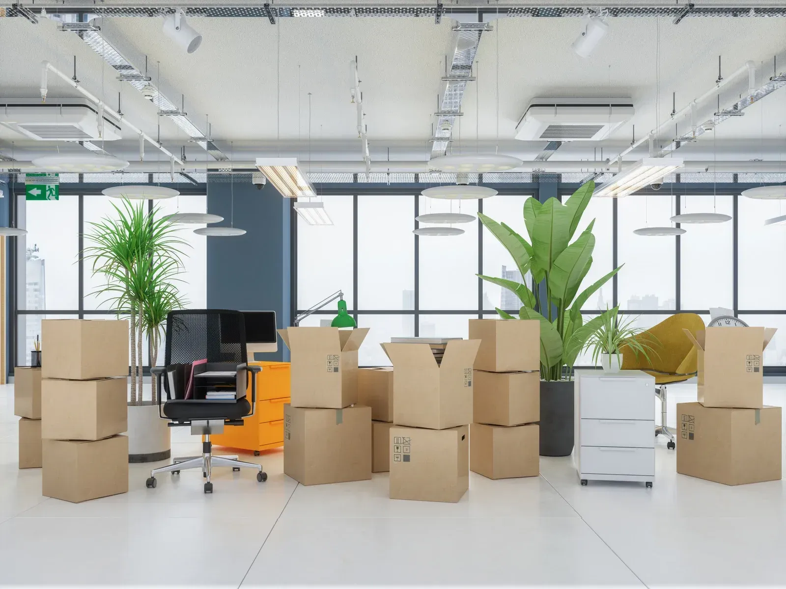Office relocation: Cardboard boxes stacked amidst furniture and plants, near large windows.