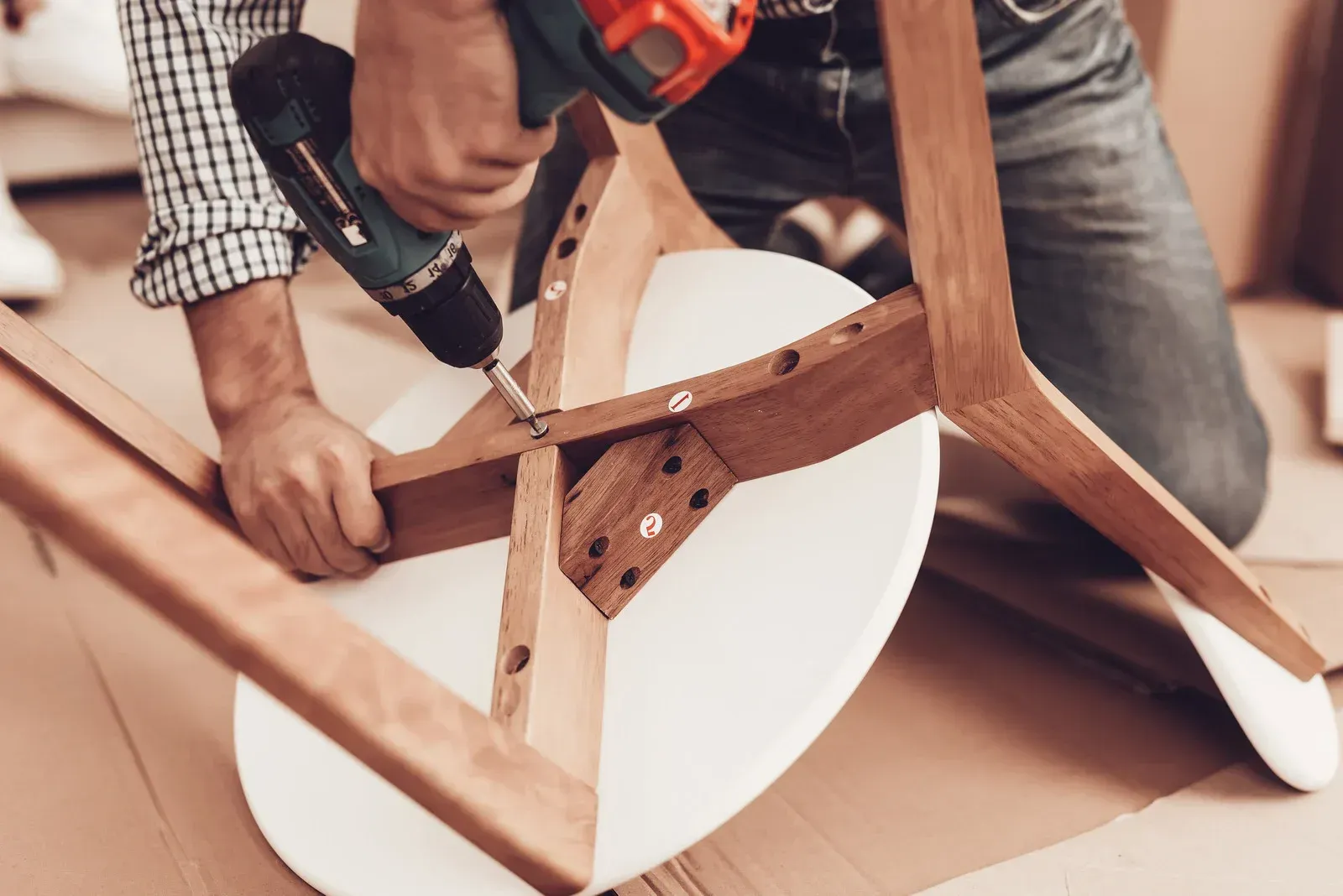 Person using a power drill to assemble a wooden chair.