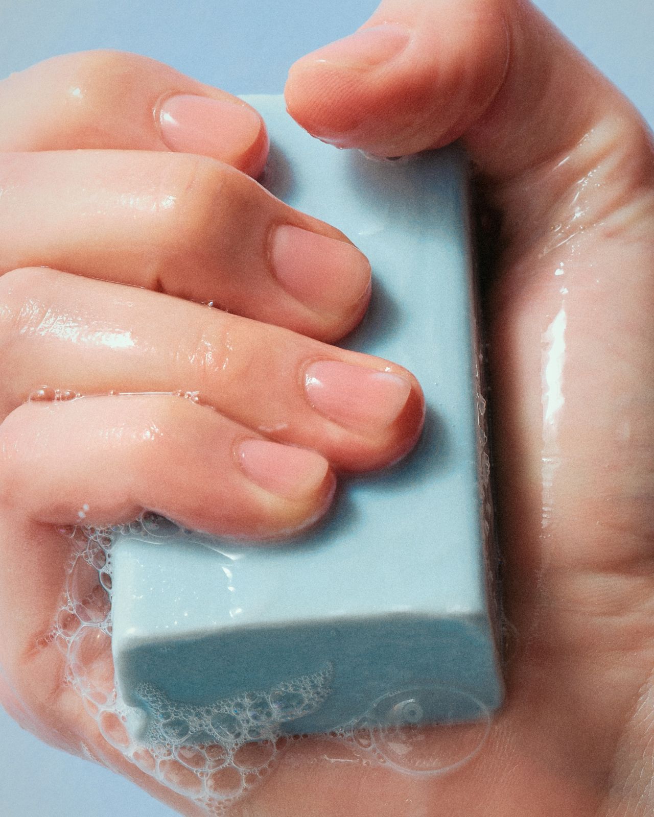 Hands holding a blue soap bar with bubbles and lather.