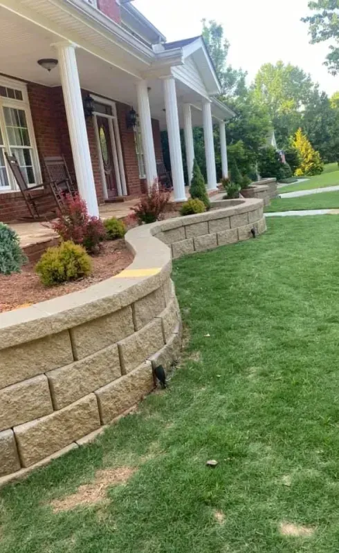 Brick house porch with white columns, curved stone retaining walls, and a neatly landscaped lawn.
