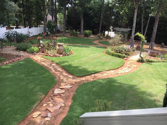 Curved stone path through a landscaped green garden with flower beds and trees