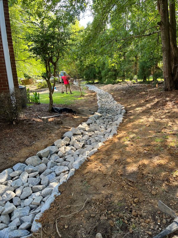 Wooded trail with a winding white rock drainage bed and a person in a red shirt in the distance