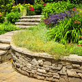 Stone garden steps beside a curved retaining wall with lush green plants and purple flowers