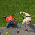 Worker edging a lawn with a red machine beside a gravel path and green grass.