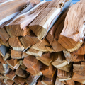 Stacked split firewood logs with rough bark and light brown wood grain.