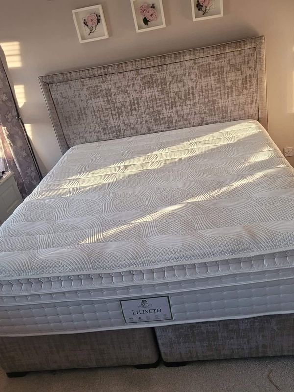 Bedroom with a large bed, patterned headboard, and white quilt in soft sunlight.