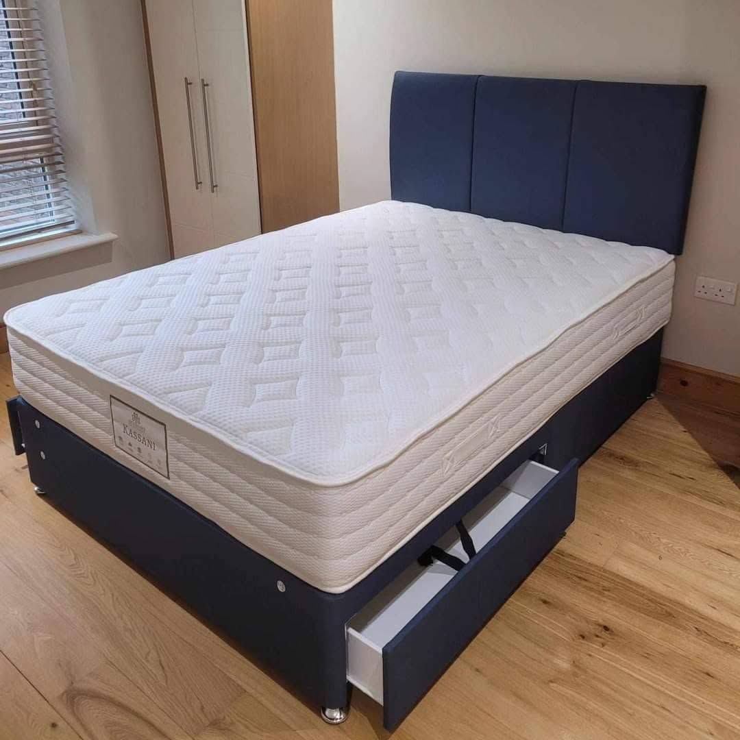 White mattress on a black storage bed frame with blue upholstered headboard in a bright bedroom