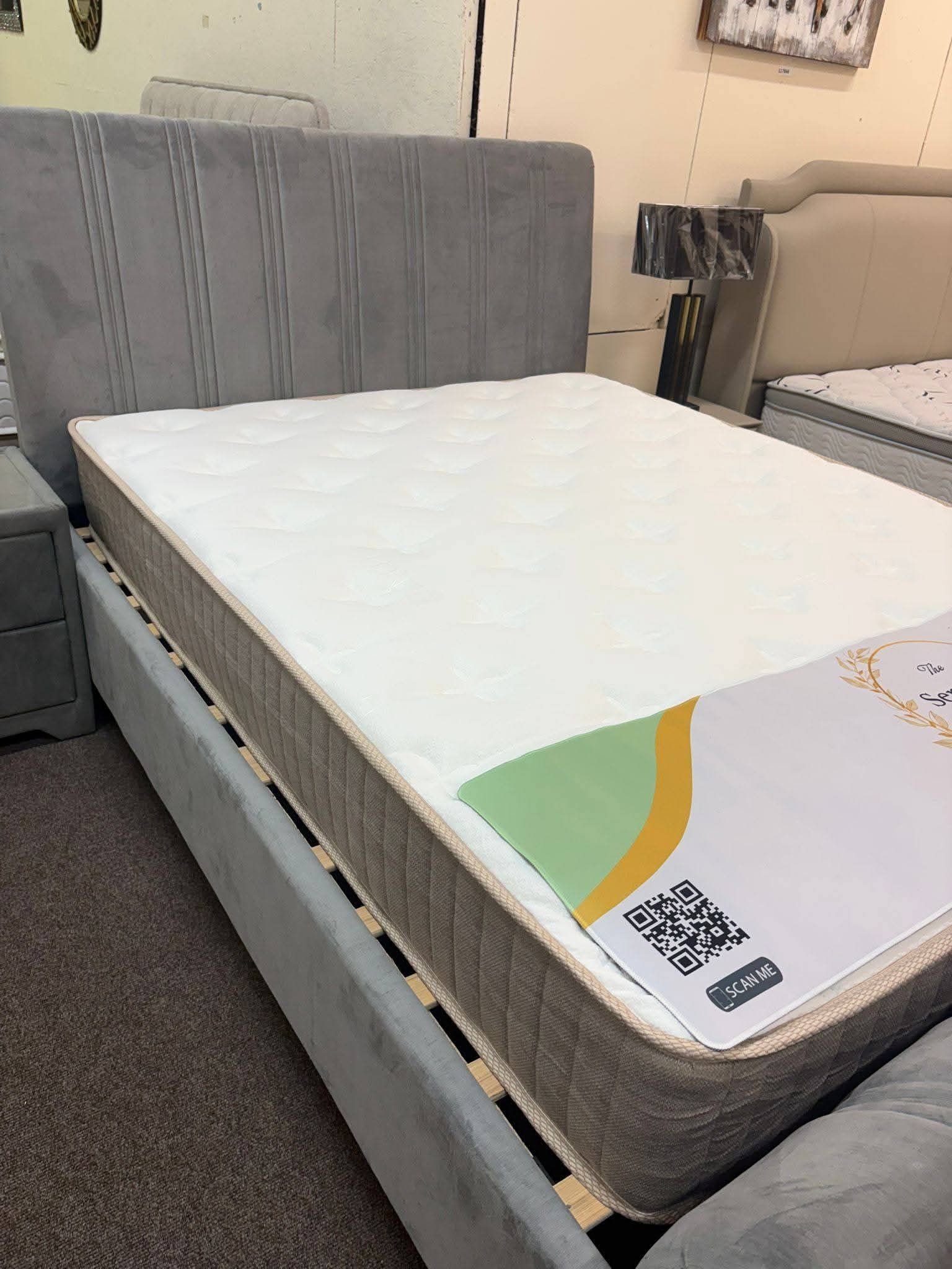 Mattress on a gray upholstered bed frame in a bedroom, with a white top and colorful corner label