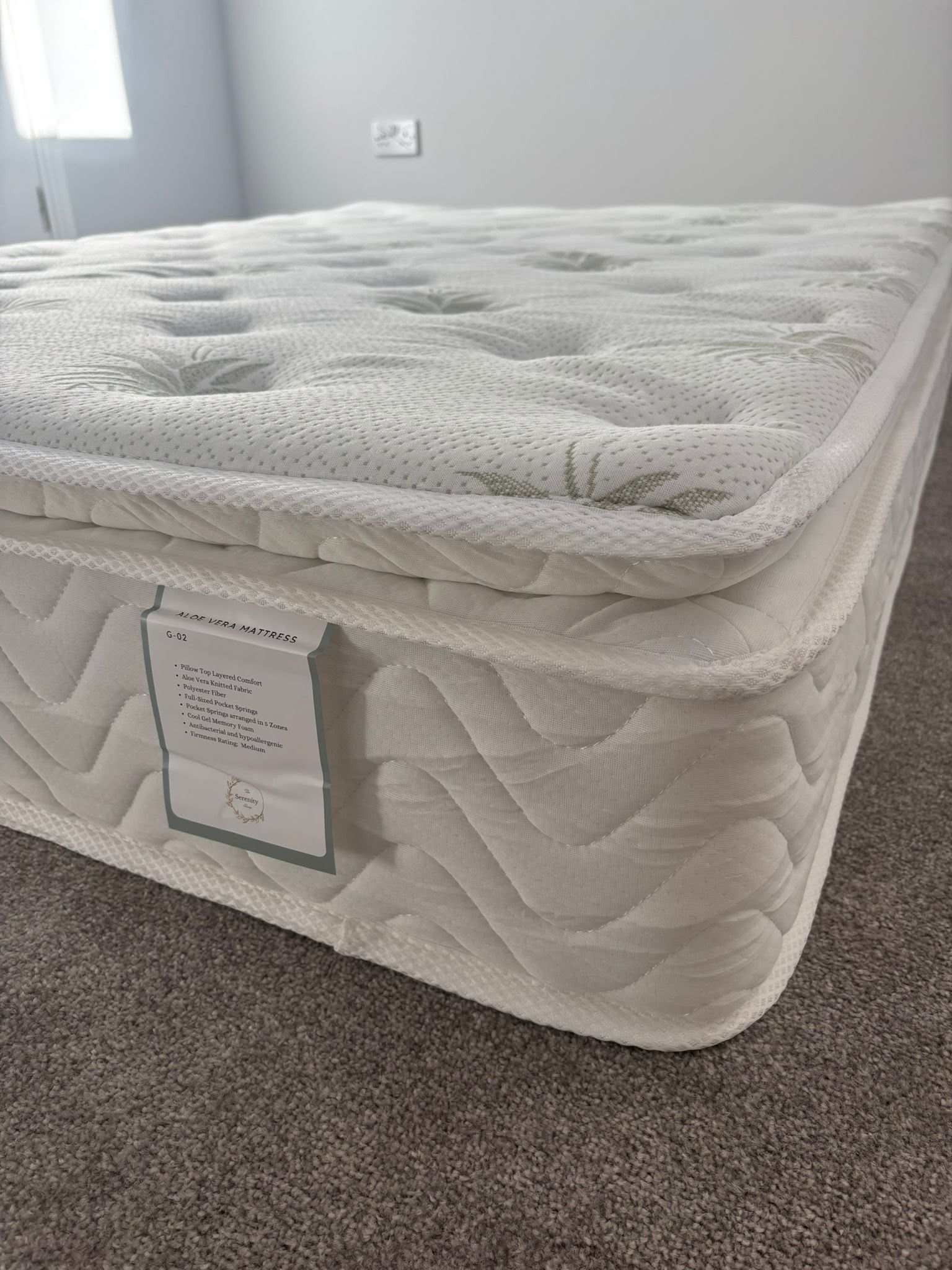 White mattress on carpeted bedroom floor, with a quilted topper and product tag on the side.
