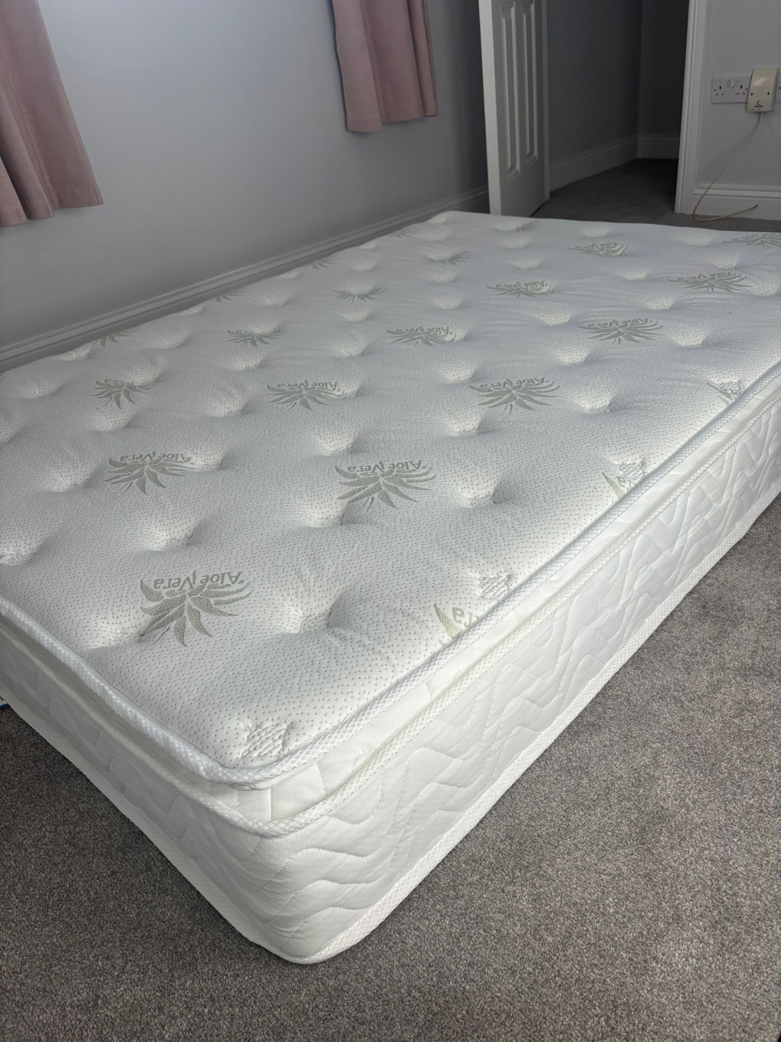 White mattress on carpeted bedroom floor near curtained window and open door
