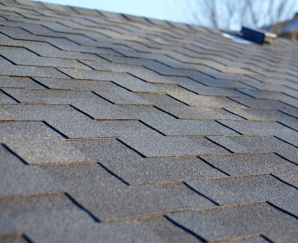 Close-up of gray asphalt roof shingles with a small vent near the ridge