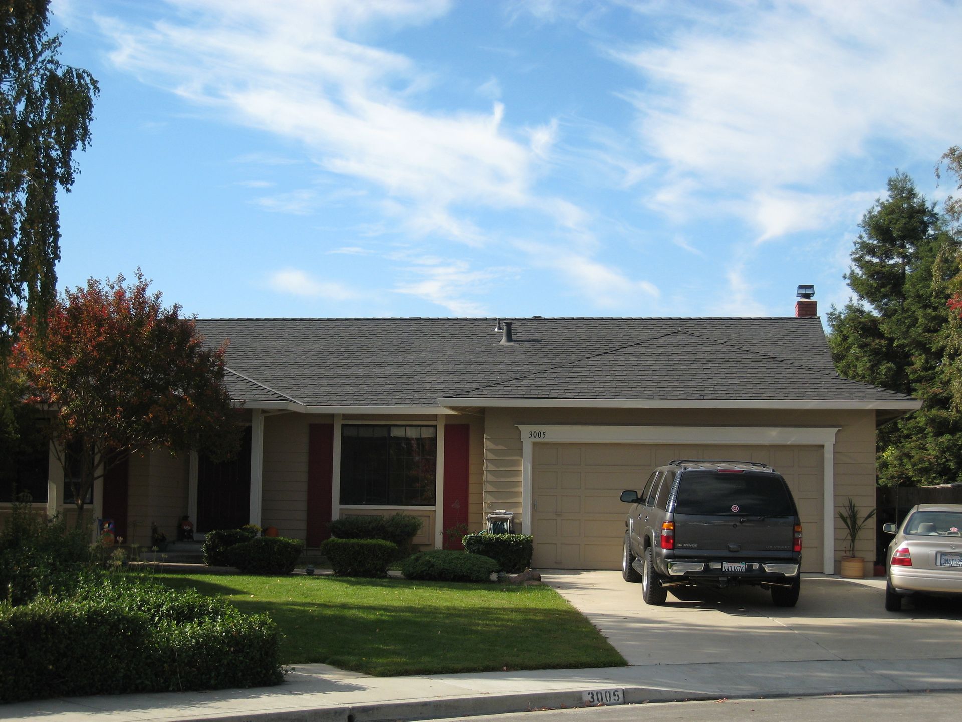 Single-story suburban house with two cars parked in the driveway under a blue sky.