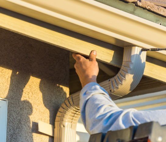 Person inspecting gutter downspout and roof edge on a house in daylight