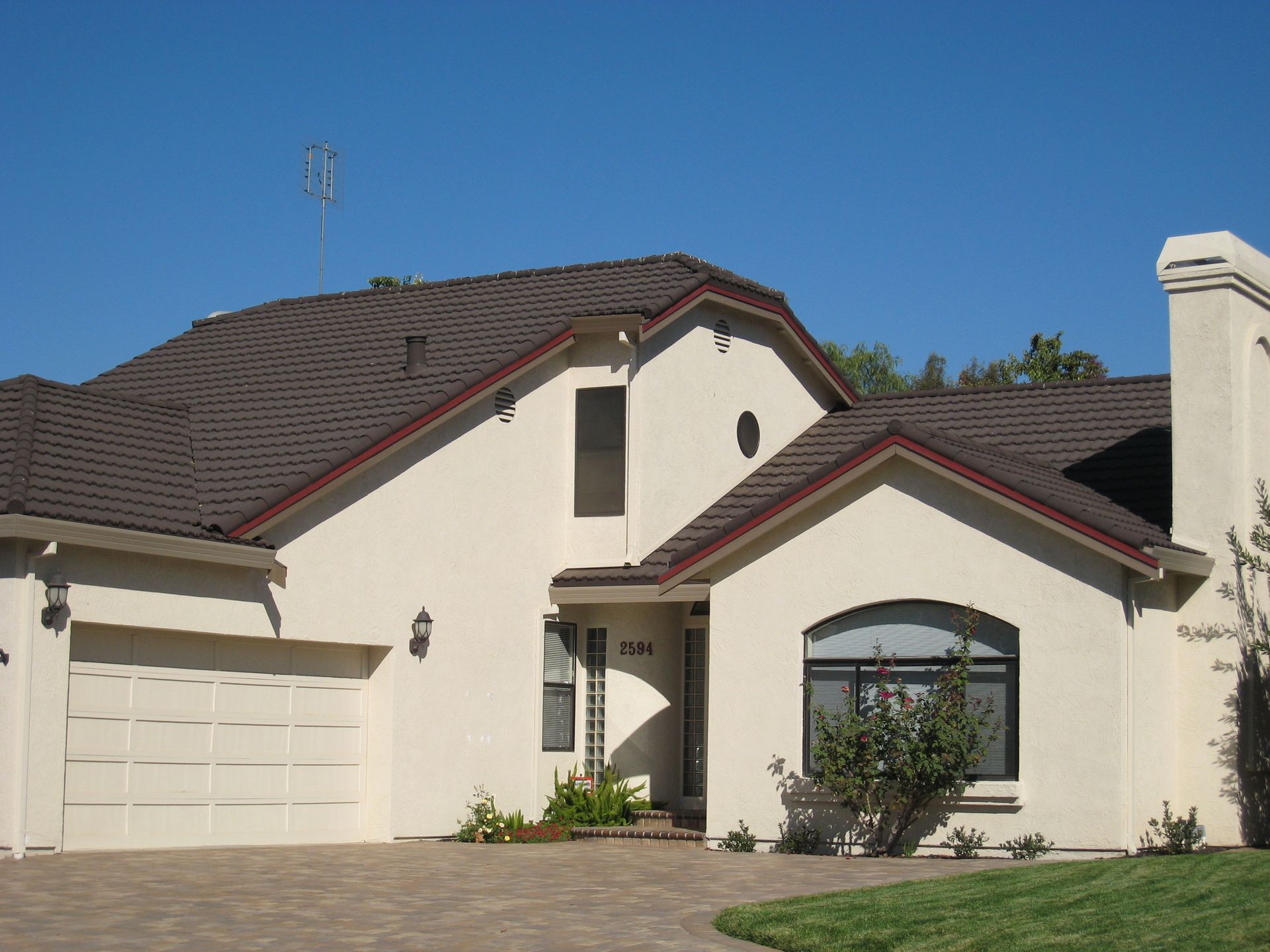 Suburban house with beige stucco walls, dark tiled roof, and a two-car garage under a blue sky