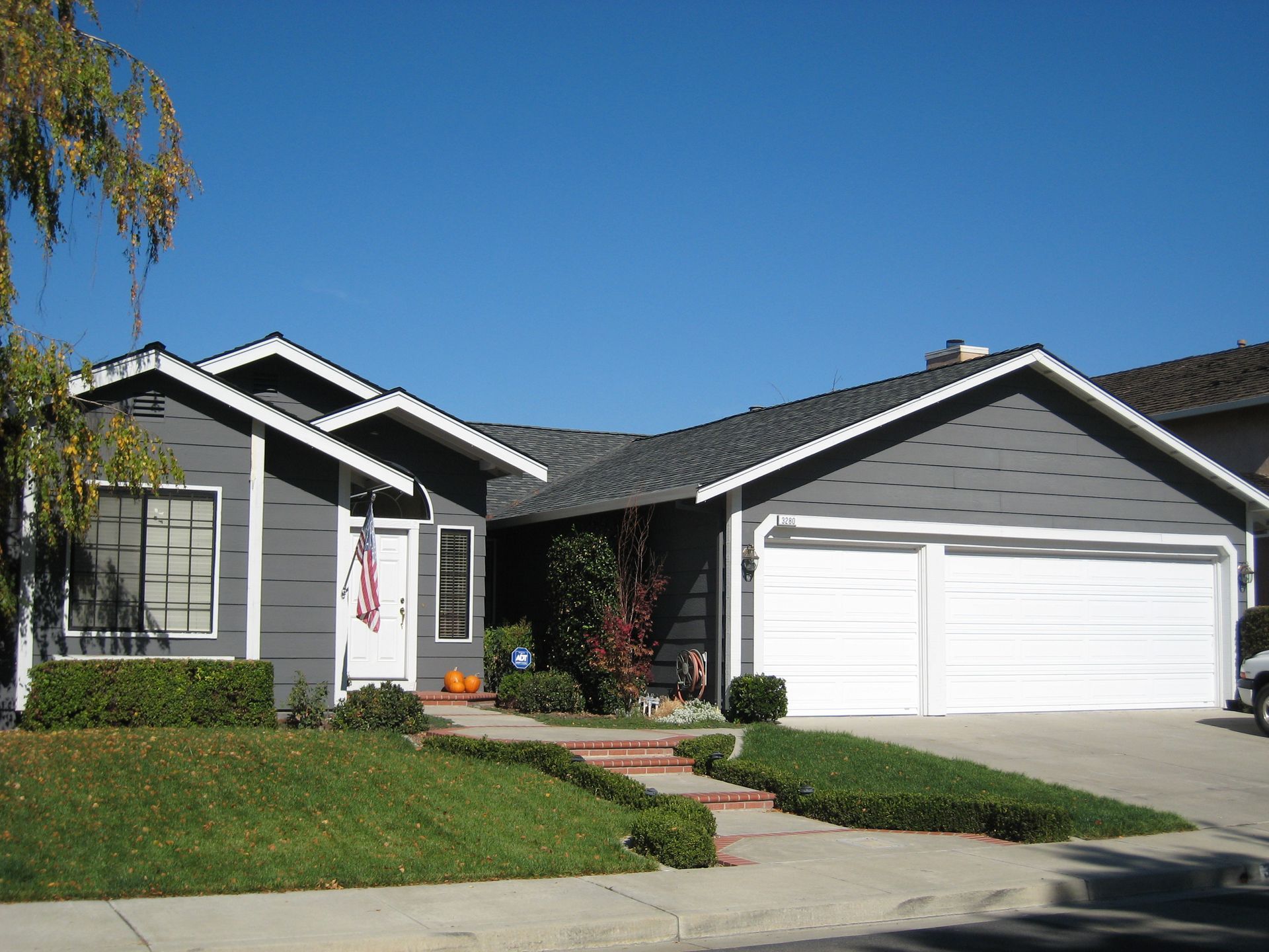 Suburban single-story house with gray siding, white garage, green lawn, and clear blue sky