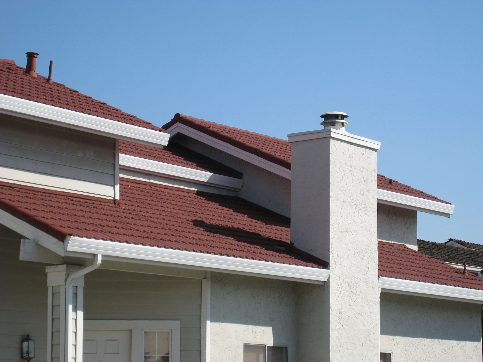 Residential rooftops with red shingles and a white chimney against a clear blue sky