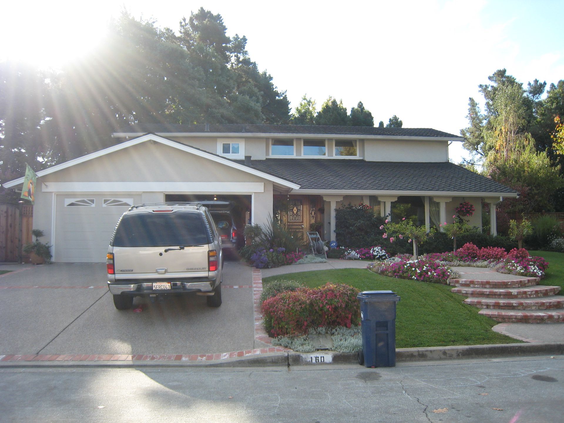 Suburban house with a beige SUV in the driveway, front porch, and flower beds at sunset