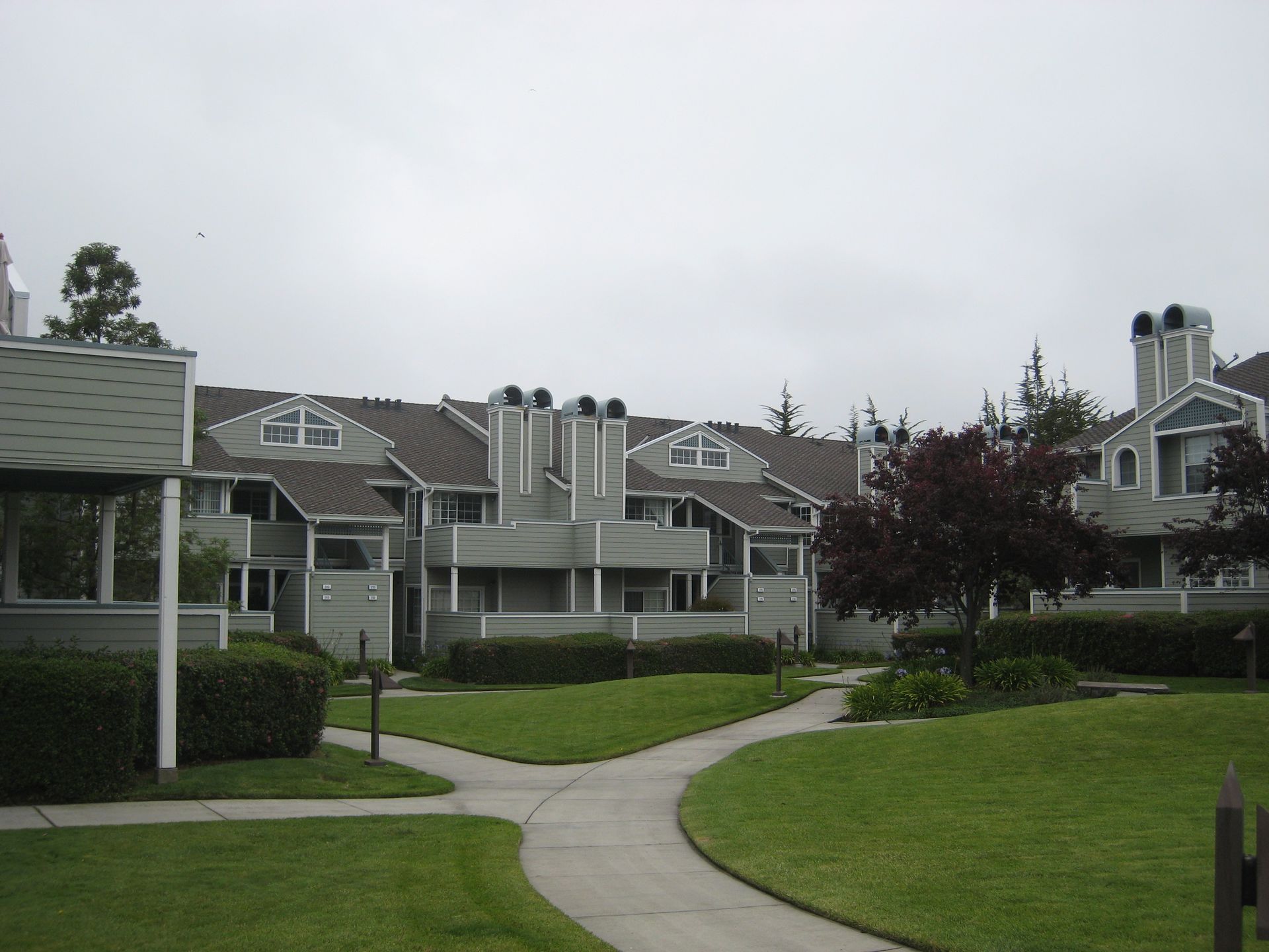 Apartment complex courtyard with curving sidewalks, manicured lawns, and gray townhouses under an overcast sky