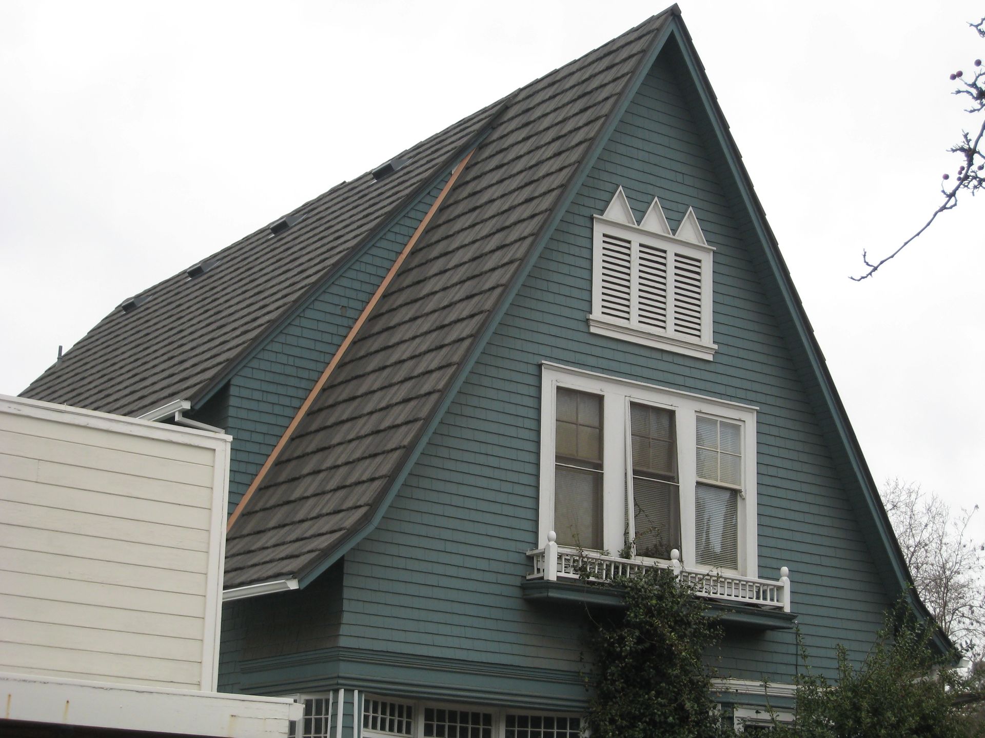 Teal house with steep dark roof and white-trimmed windows, viewed from below