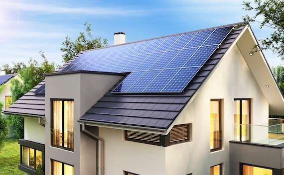 Modern house with large blue solar panels on the roof in a bright suburban setting