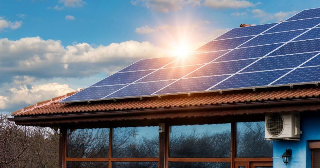 Solar panels on a rooftop at sunrise above a blue building with cloudy sky.