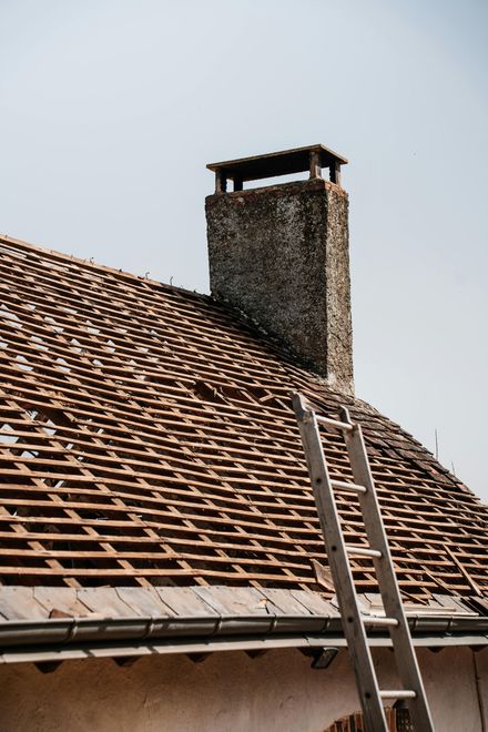 Tile roof with a brick chimney and metal ladder under a clear sky