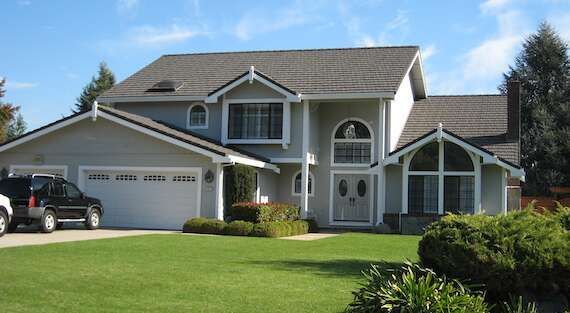 Suburban two-story house with a white garage, manicured lawn, and parked car in the driveway