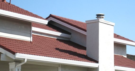 Red-tiled house roof with white chimney against a blue sky