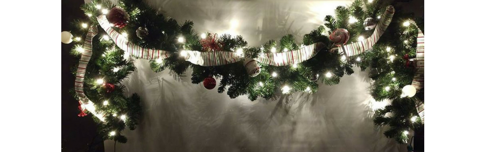 Holiday garland with white lights and red accents draped over a mantel in a dim room