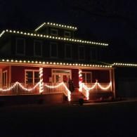House outlined with warm white holiday lights at night, with glowing garlands across the porch.