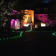 House lit with pink and amber lights at night, with green pathway lights leading to the entrance.