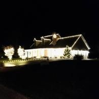 House outlined in white Christmas lights at night, with lit trees in the front yard.