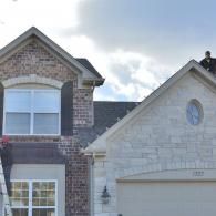 Suburban brick and stone house facade with gabled roof and garage under a partly cloudy sky
