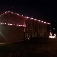 House outlined with pink Christmas lights at night, with a lit white tree decoration in the yard.