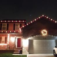 House decorated with red holiday lights and a wreath above the garage at night
