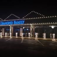 Nighttime exterior of Diamond Family store with blue sign and white holiday lights on the facade.