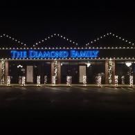 A lit storefront at night with blue sign reading “THE DIAMOND FAMILY” and string lights on the roof.