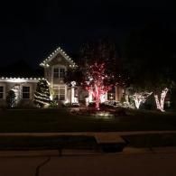 House decorated with white Christmas lights and a red-lit tree at night