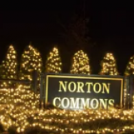 Norton Commons sign lit by warm white holiday lights at night