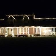 House at night with warm white string lights along the roof and porch