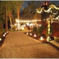 Candlelit garden path at night with string lights and lanterns along a fence and trees