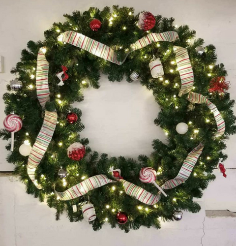 Decorated Christmas wreath with white ribbon, red ornaments, and lights on a wall