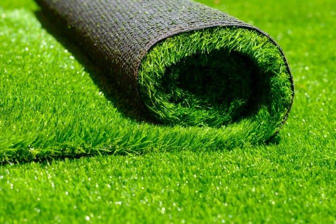 A roll of artificial green grass partially unrolled on a flat, grassy lawn.